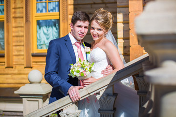 Beautiful bride and groom standing on stairs on background of country house