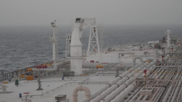 Deck of very large tanker, seaman walks, haze in Persian gulf.