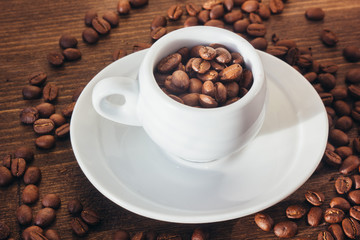 Coffee beans on white coffee cup over the wooden table.
