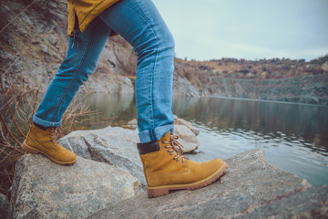 Female legs in jeans and hiking boots near edge of mountain lake.