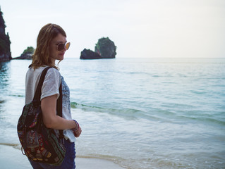 Beautiful girl in glasses with a backpack on the background of sea and sky. Behind the mountains and the horizon. Sunny day, tourism, leisure