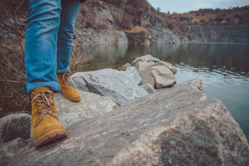 Female legs in jeans and hiking boots near edge of mountain lake.
