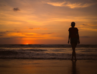 Fototapeta premium Young beautiful slim girl on the beach watching the sunset and the horizon. Sea sunset landscape
