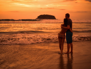 Young beautiful couple on the beach watching the sunset and the horizon. Seascape. Beautiful man and woman near the ocean at sunset