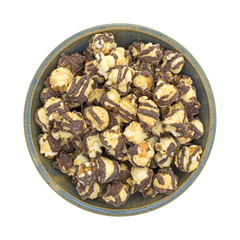 Fudge drizzled popcorn in an old bowl top view isolated on a white background.
