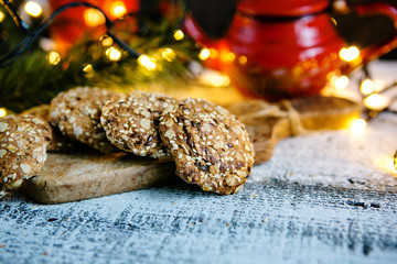 New Year cookies with sesame seeds and grains on a background of luminous garlands and red teapot,...