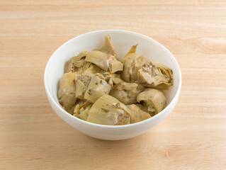 Marinated artichoke hearts in a bowl atop a table.