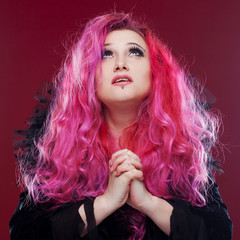 Fototapeta premium Scary witch with red hair folded her hands in prayer. Looking up