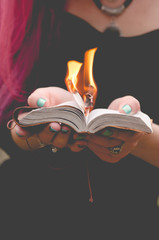 Obraz na płótnie Canvas Young witch with pink hair is burning pages of her spellbook