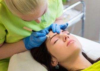 cosmetologist preparing young woman for permanent eyebrow make u