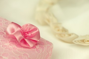 Close-up of a pink present box with a flower and a wedding flower wreath in the background