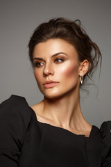 Fototapeta premium Portrait of a beautiful, self-sufficient and confident young woman with collected hair in the elegant black dress with makeup, dark background, studio photo