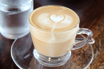 Hot cappuccino coffee with heart shape in clear glass.