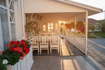 Flowers hanging on a porch. White colored house and sunlight. Time to come back home. Remember those who await you.