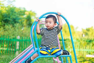 Sad little Asian kid sitting on slide at the playground at the d