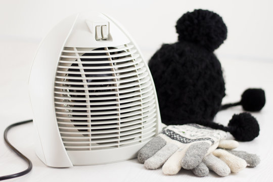Electric fan heater warming room in winter, gloves and wool hat on white floor isolated