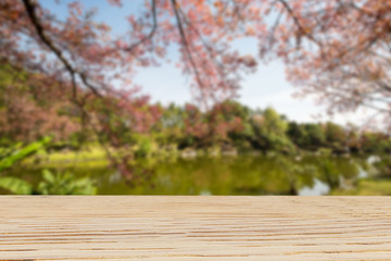 Naklejka na ściany i meble Wooden table top on blurred cherry blossom tree and lake background