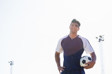 Happy football player standing with a ball