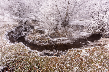 Winter Creek bed. Creek that flows in the creek bed, covered of snow in winter and the ice coast.