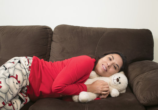 Mujer acostada en sill&oacute;n con oso de peluche