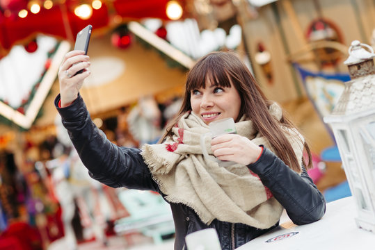 beautiful woman drinks mulled wine and makes a selfy on mobile p