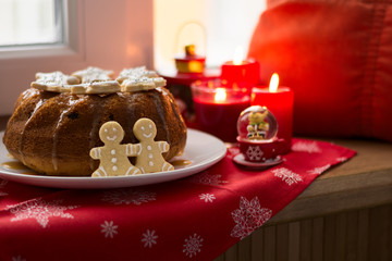 Christmas decoration: cake, gingerbread-men and burning red candles on windowsill