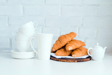 Piece of kitchen restaurant interior. Pile of baked croissants on wooden board and stack of cups, teapot. White background. Copy space.