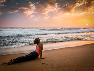 Fototapeta na wymiar Woman practices yoga asana Urdhva Mukha Svanasana at the beach
