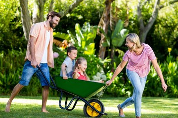 Parents pushing children sitting in wheelbarrow at yard  