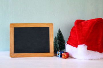 Obraz na płótnie Canvas christmas trees and santa hat next to blank blackboard