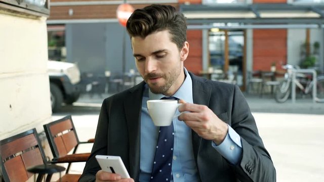 Businessman drinking coffee and reading something on smartphone
