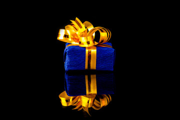 blue gift box with gold ribbon on a black background with reflection