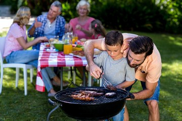 Father teaching son cooking on barbecue with family 