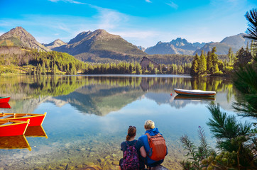 Young couple on the shore of beautiful lake under mountains. Original wallpaper from summer morning