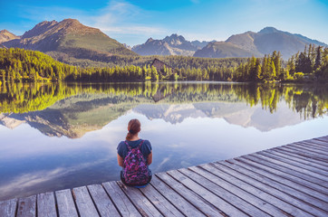 Alone young girl sitting and resting on the wooden path near by beautiful blue lake and clear big...