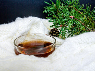 Glass cup of hot tea, dressed in knitted warm scarf winter warm knitted sweater or blanket. Still scarf and a cup of tea with Christmas tree. In the winter time. Cozy and soft winter background.