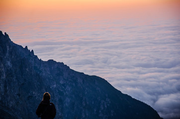 Obraz premium Young girl looking at beautiful scenery. Clouds are in the valley before the sunrise