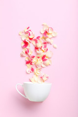 Fototapeta na wymiar Rose petals and white cup on a pink background