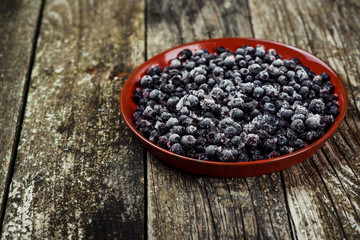 Frozen blueberries in a bowl on wooden background. Selective focus.