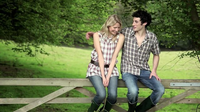 Young couple sitting on gate in countryside