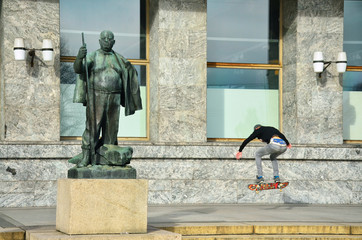 Young man jumping on skateboard in oslo near by statue of fat man

