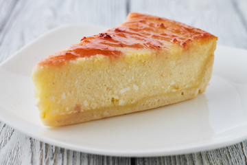 Slice of the New York cheesecake on a white plate on a wooden background
