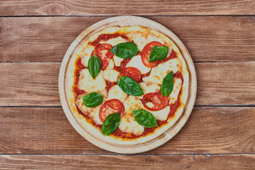 Pizza Margherita with tomatoes, mozzarella and basil on a wooden background сlose up.