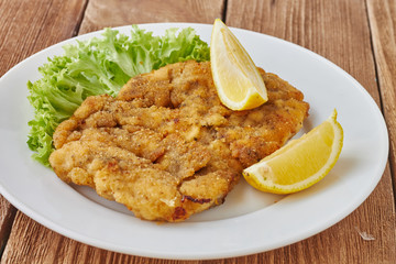 Weiner schnitzel with green salad and lemon on a wooden background