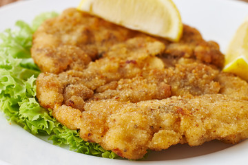 Weiner schnitzel with green salad and lemon on a wooden background
