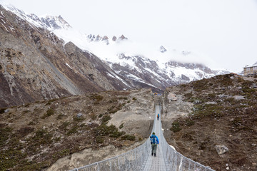 Trekker walking on the hanging bridge over the cliff on the way to Thorong Phedi, Annapurna...