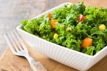 Kale salad in bowl with carrot, pepper and sweet corn on wooden background

