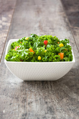 Kale salad in bowl with carrot, pepper and sweet corn on wooden background
