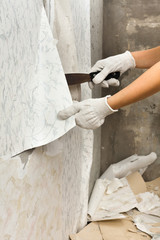 hands removing old wallpaper from wall