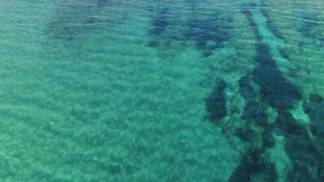 Aerial of clear seawater, camera rising to reveal boat and coastline of Greek island of Paros.
